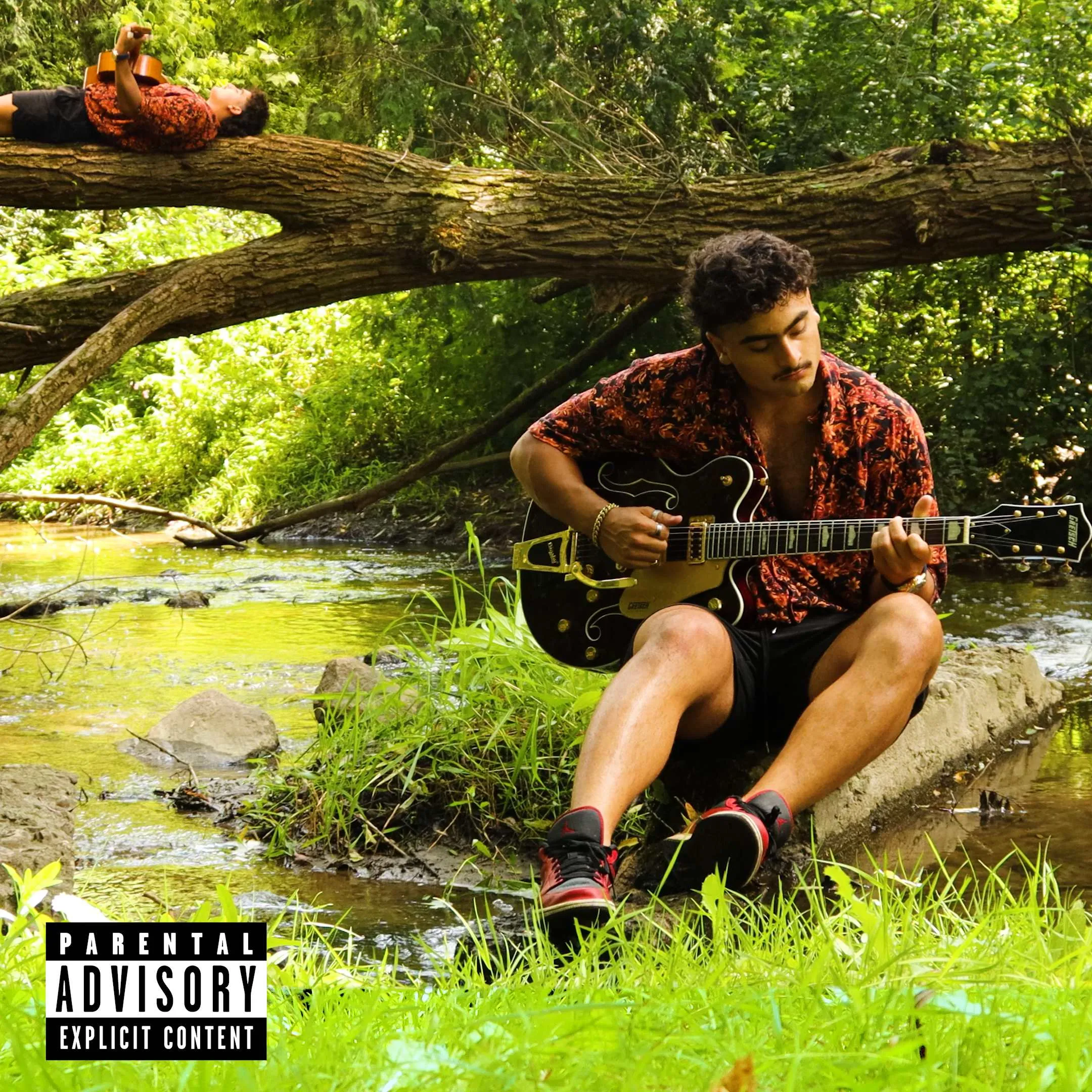 Noam Miko playing guitar by a stream